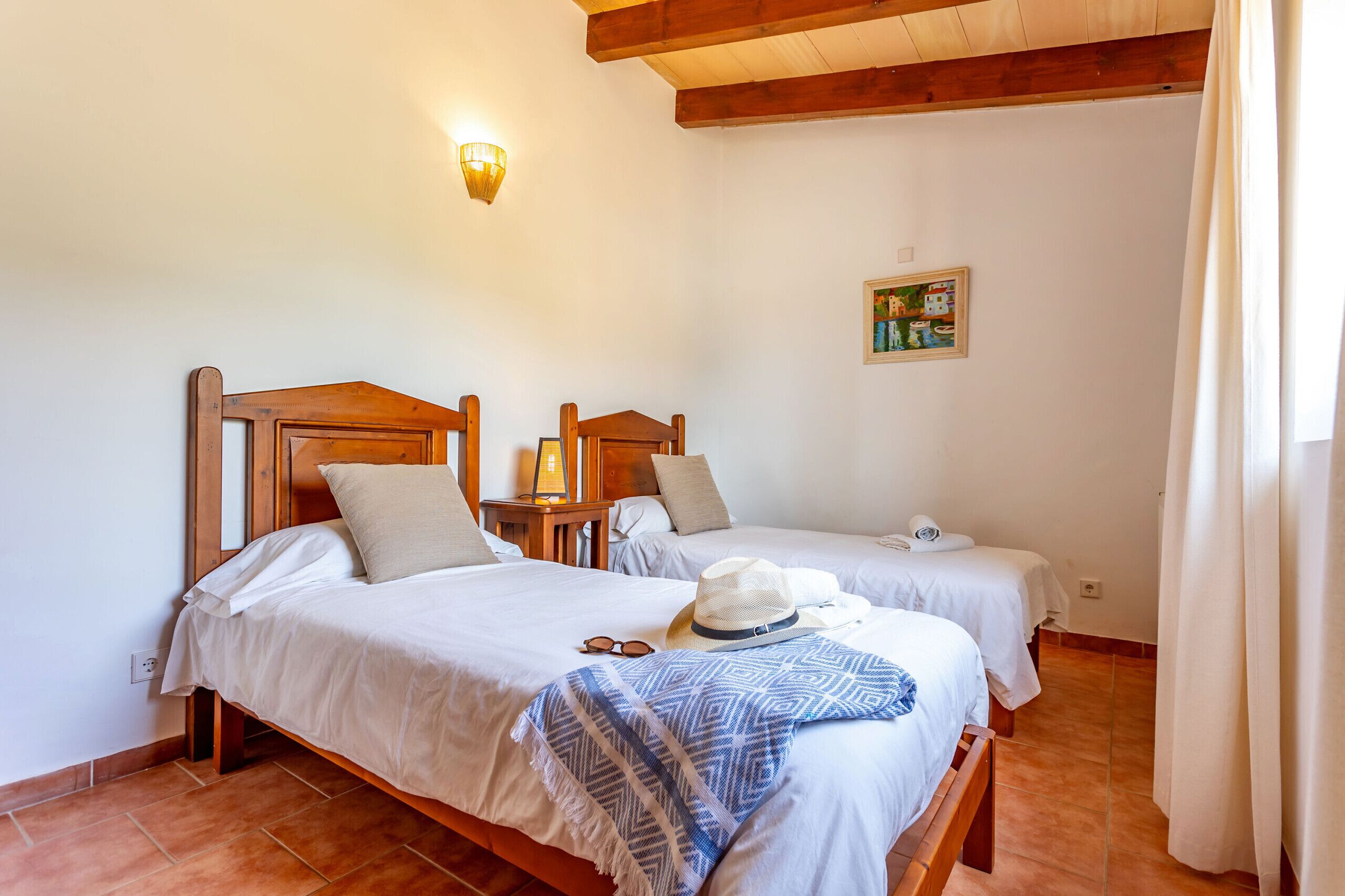 Habitación con dos camas, cabeceros de madera, una lámpara de pared y un cuadro pequeño.