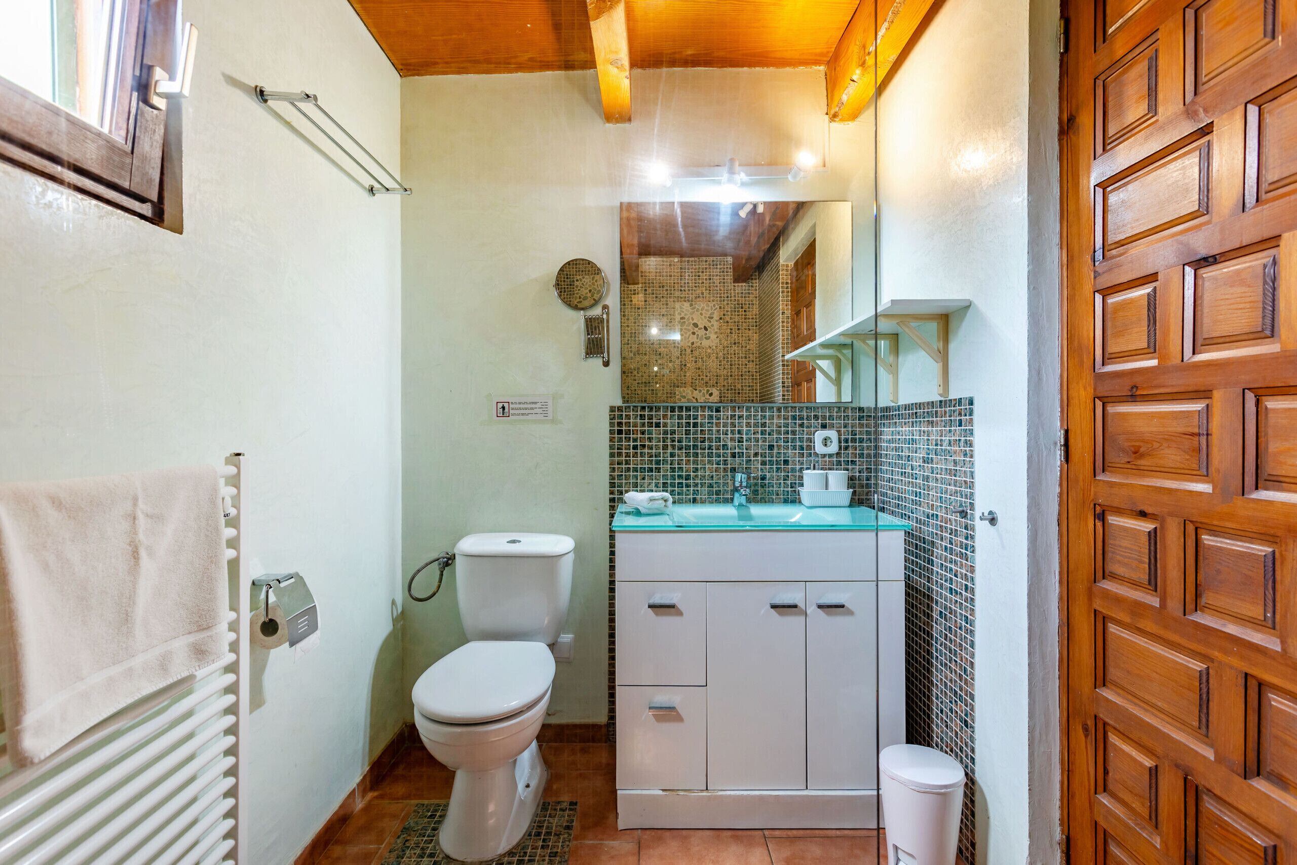 A compact bathroom with a white toilet, a white sink with a glass countertop, and a wooden door.
