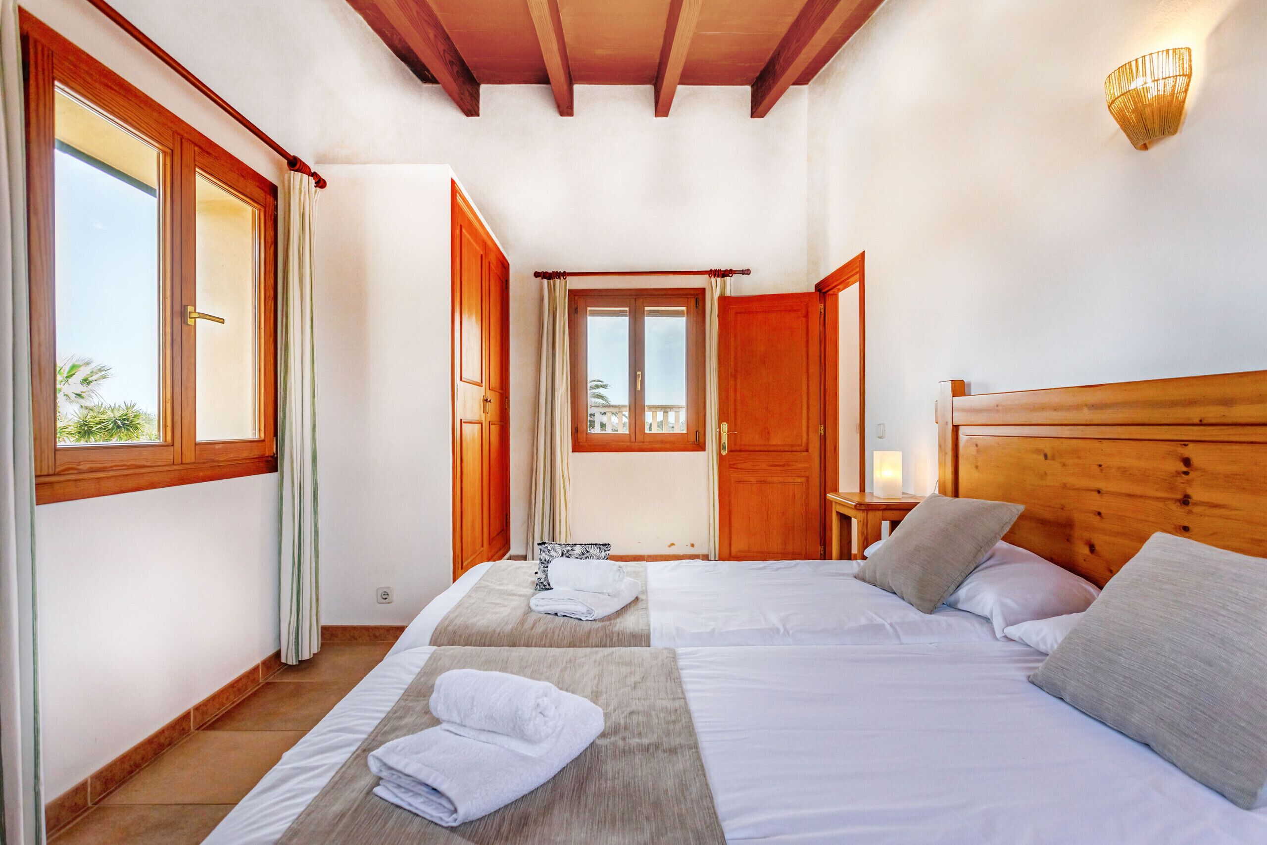 Une chambre d’hôtel avec deux lits, des têtes de lit en bois, un plafond en bois, une fenêtre avec des rideaux et une table de chevet avec une lampe.