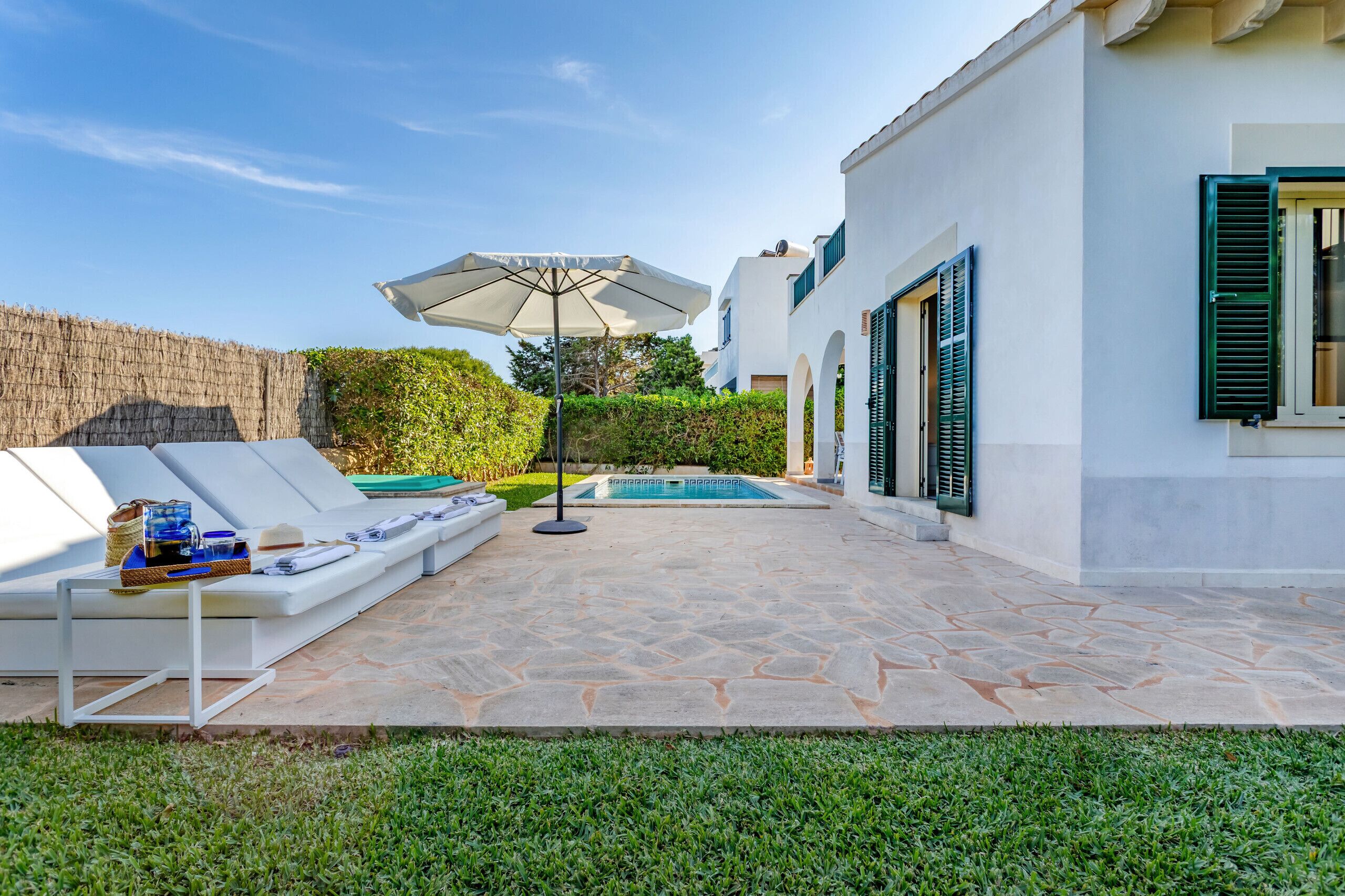 A poolside area with lounge chairs, a sun umbrella, and a stone patio.