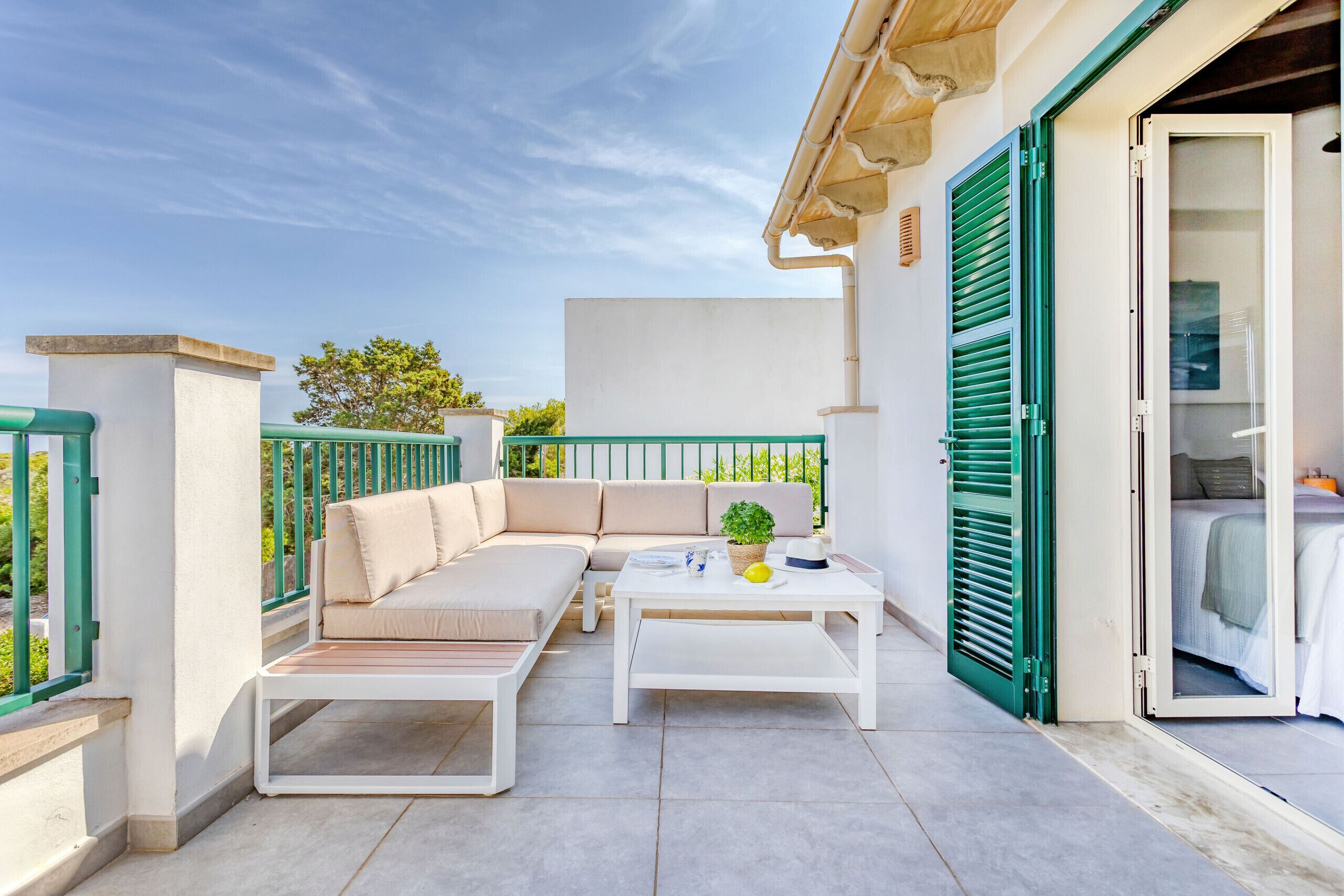 A balcony with a beige sofa, a white coffee table, and a potted plant.