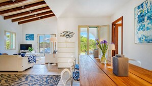 A modern living room with a wooden ceiling, white furniture, a dining table, and a view through a glass door. - Can Sivinar by dracmallorca (Santanyi)