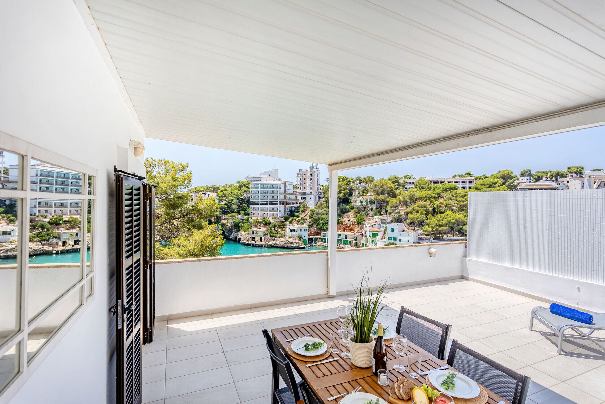 Ein Balkon mit Esstisch, mit Blick auf eine Küstenstadt und türkisfarbenes Wasser.