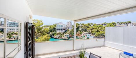 Ein Balkon mit Esstisch, mit Blick auf eine Küstenstadt und türkisfarbenes Wasser.