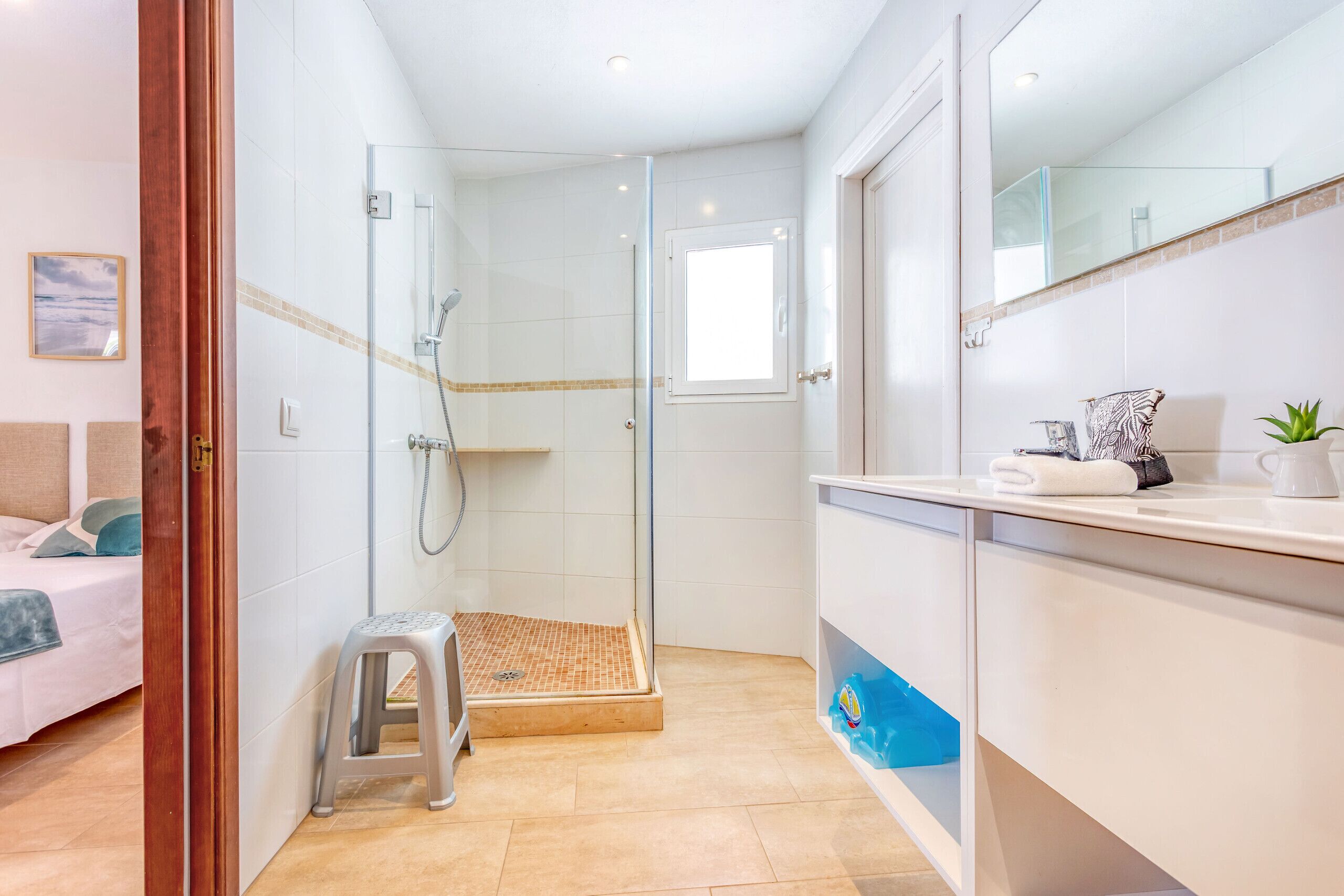 A modern bathroom with a glass shower enclosure, a small stool, and a vanity with a mirror.