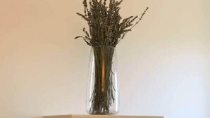 A tall, narrow wooden cabinet with wicker baskets and a clear glass vase containing dried plants on top.