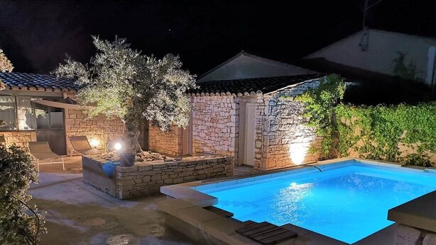 A swimming pool with stone walls and a pergola, surrounded by potted plants and a stone patio.