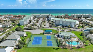 A resort with multiple tennis courts, a swimming pool, and a view of the ocean.