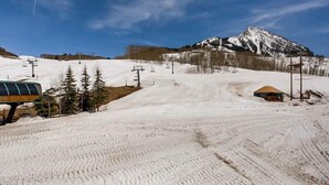 Una pista de esquí nevada con un telesilla, árboles y una montaña al fondo.