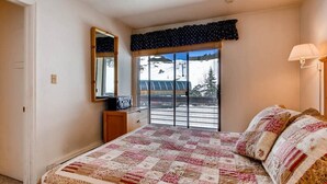 Un dormitorio con una cama grande, un aparador, un espejo, una ventana con vistas a un paisaje nevado y una lámpara.