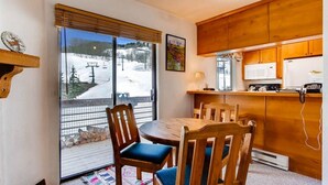Una cocina acogedora con armarios de madera, una mesa de comedor con sillas, un ventanal con vistas a un paisaje nevado y un refrigerador pequeño.