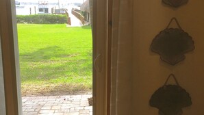 Ein Zimmer mit einer Glasschiebetür, die zu einer Wiese mit Blick auf Boote und Gebäude führt. Es sind drei dekorative Gegenstände an der Wand angebracht.