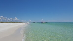 Une plage aux eaux turquoise et limpides, un rivage sablonneux et quelques bateaux.