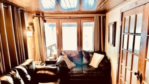 A cozy room with a leather sofa, wooden flooring, and a large window with curtains. - 220’ WATERFRONT BEACH HOME ROCK RIVER WI PETS PIER POOLS FP FISHNG BOAT KAYAKS (Edgerton)