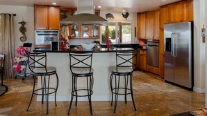 A kitchen with wooden cabinets, a stainless steel refrigerator, a built-in oven, and a bar area with stools.