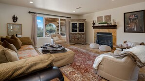 A cozy living room with a sofa, armchairs, a fireplace, and a large window with curtains.