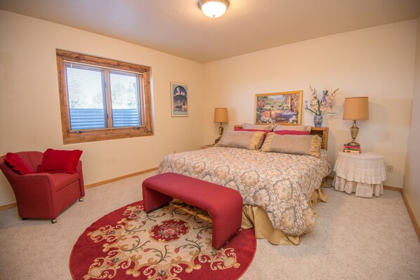 A bedroom with a bed, a red chair, a bench, a window, a painting, and a lamp.
