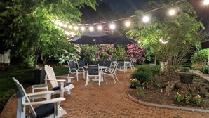 Un patio al aire libre con suelo de ladrillo, sillas reclinables blancas y un gran paraguas.