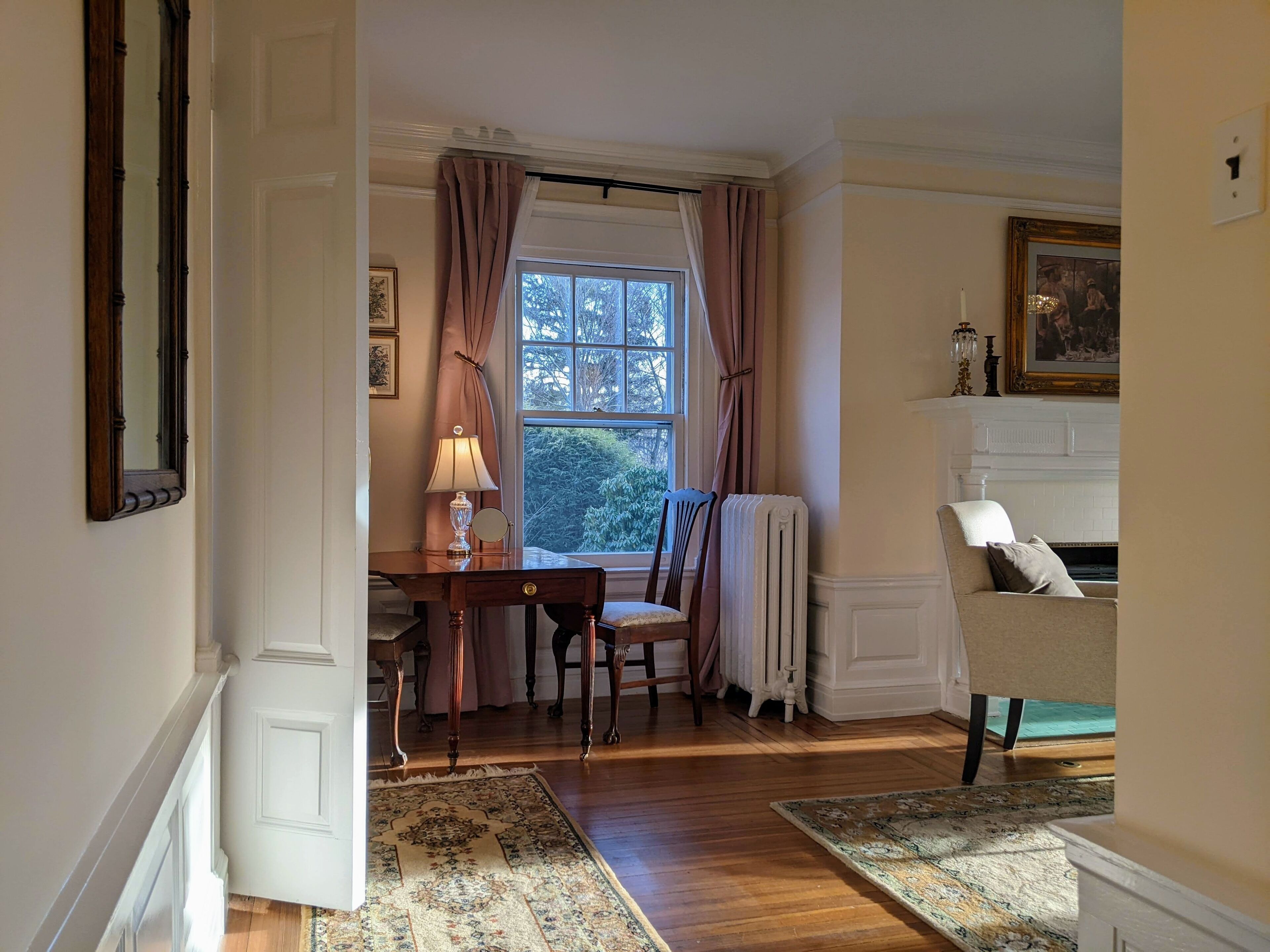 A room with a wooden floor, a table with a lamp, a chair, a radiator, and a sofa.