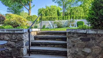 Un escalier en pierre mène à un jardin agrémenté d’une clôture blanche en bois et d’un espace aménagé pour s’asseoir à l’extérieur.