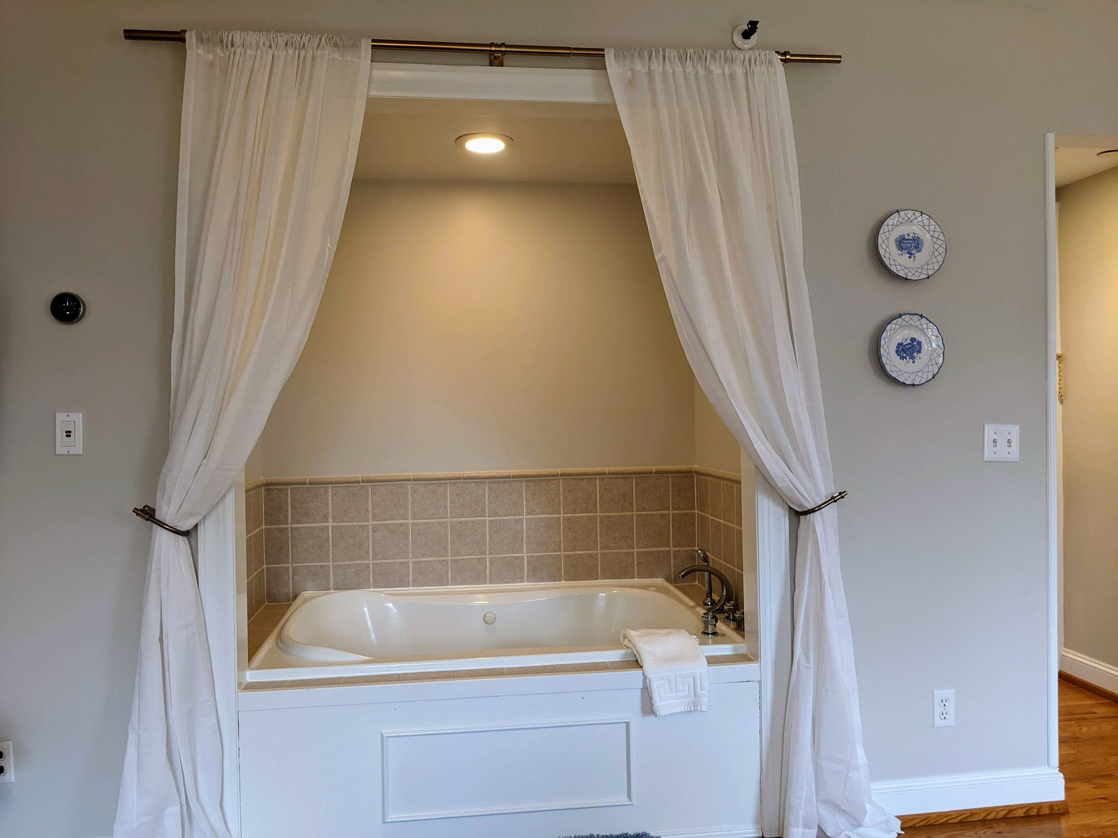 A bathroom with a bathtub, white curtains, and two decorative plates on the wall.