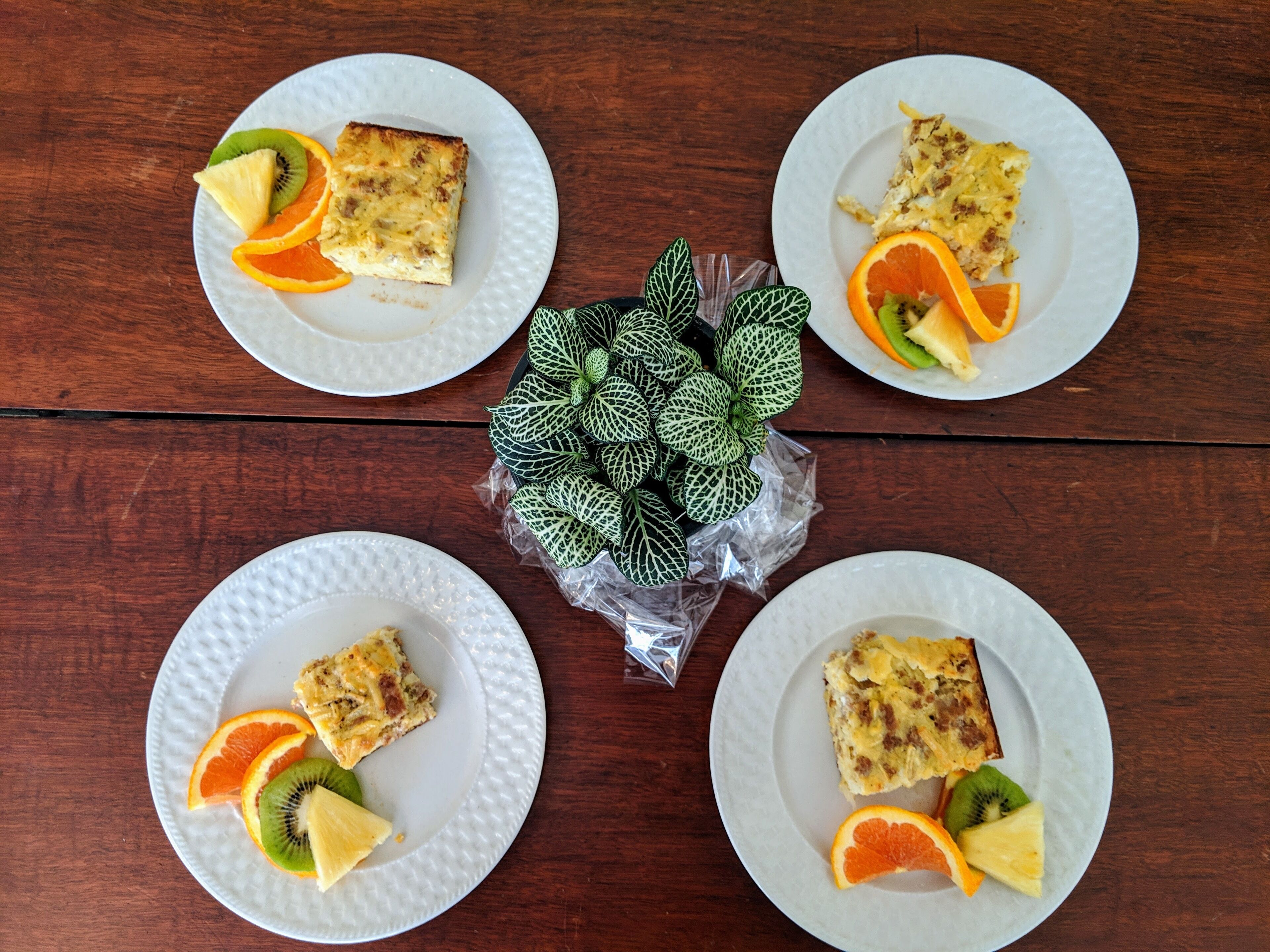 Four white plates with slices of orange and kiwi on a wooden table.