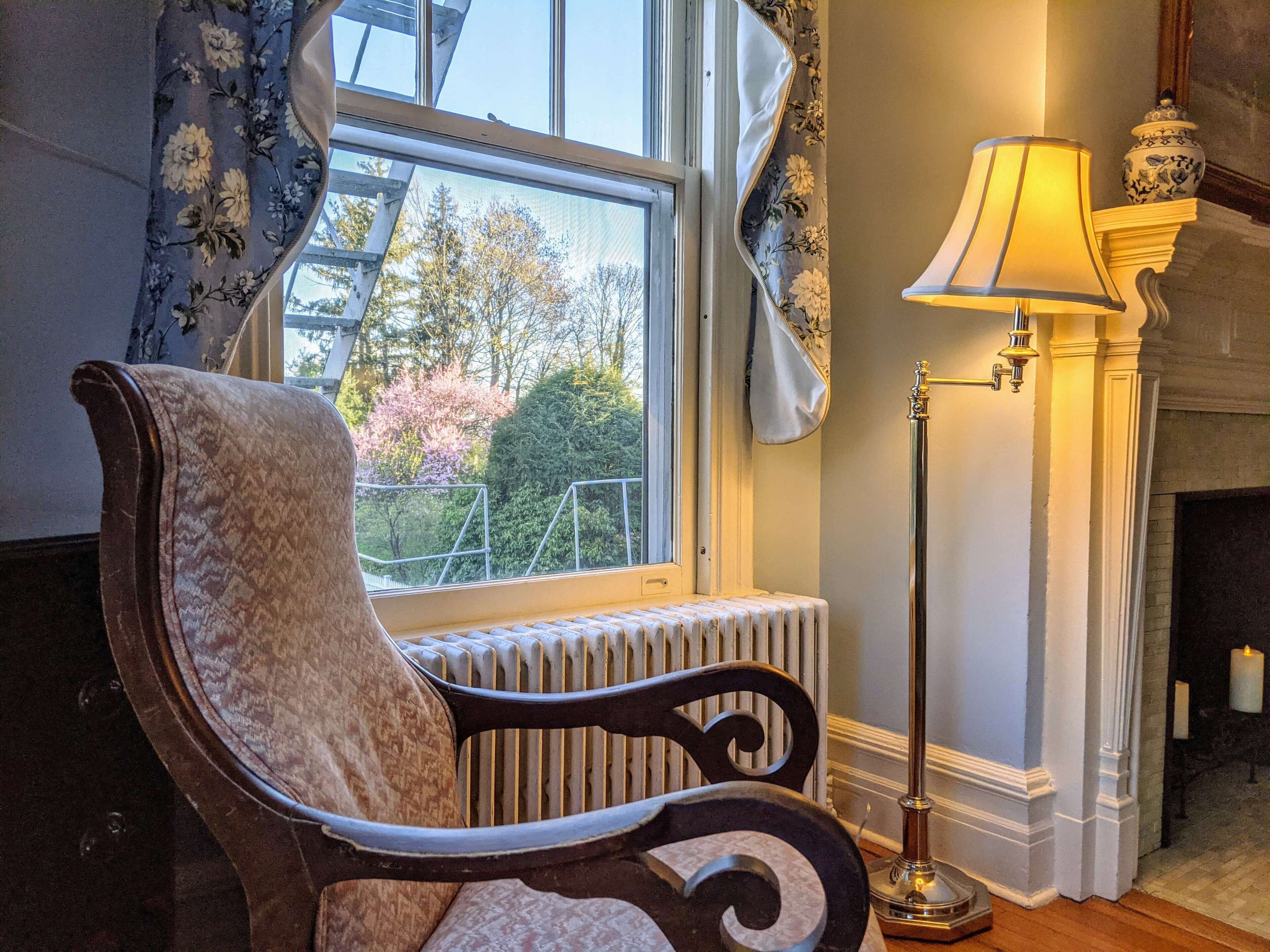 A room with a radiator, a chair, a floor lamp, and a view of trees outside.