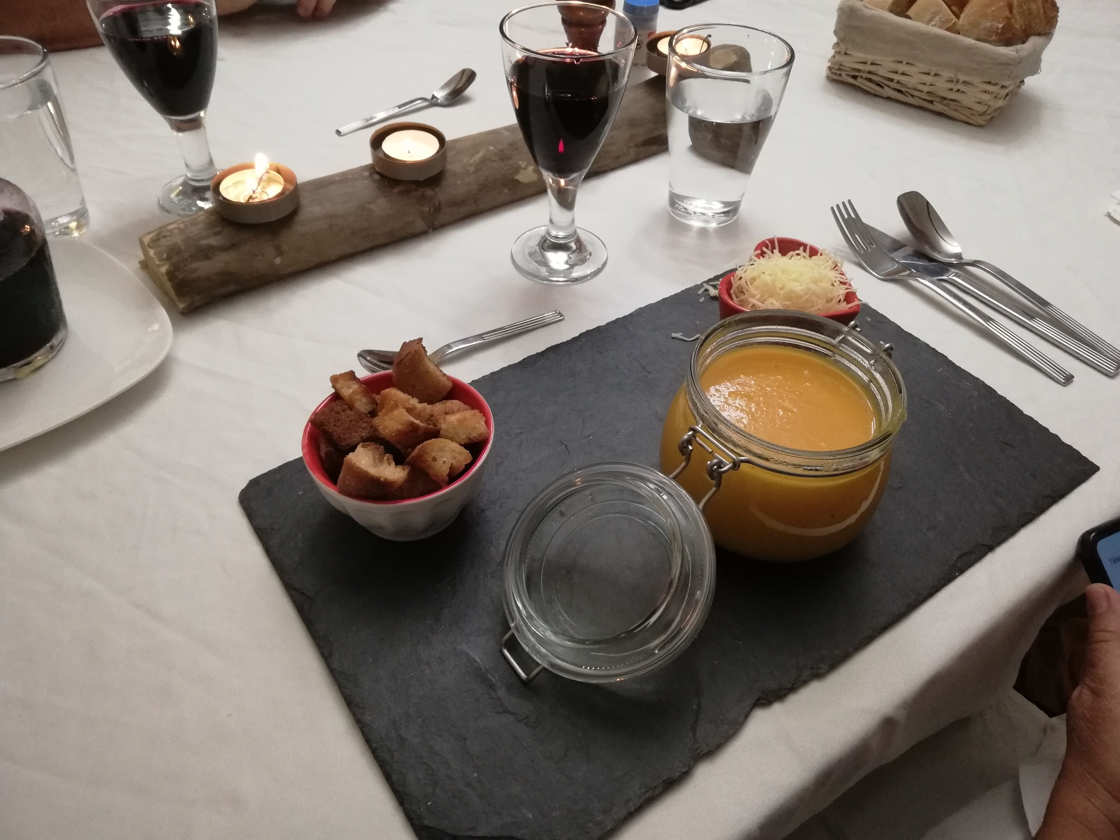 Una mesa de comedor con un tarro de salsa de naranja, un bol de croutons y una vela.