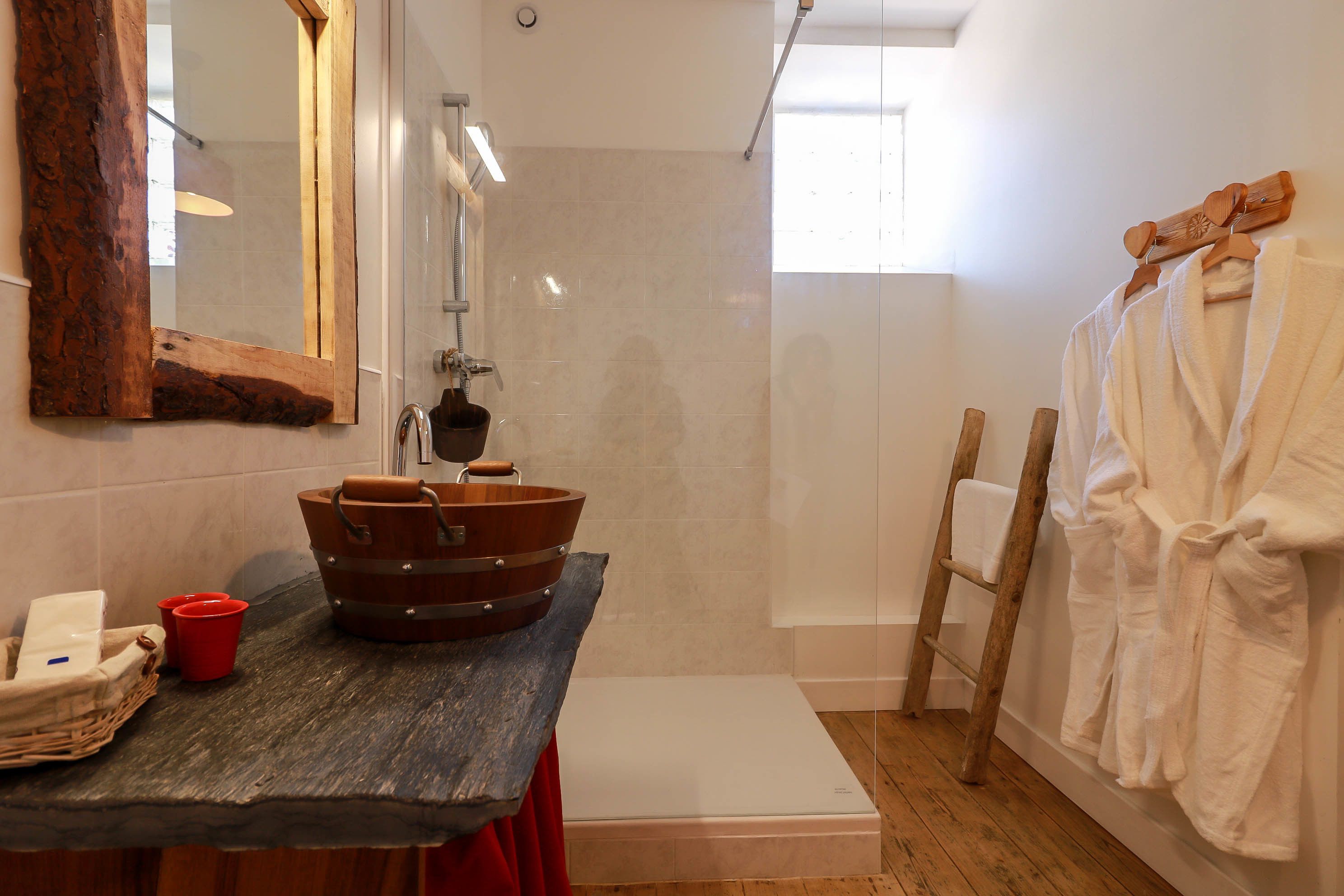 Un baño con un lavabo de madera, un espejo con marco rústico, un perchero con toallas blancas y una escalera de madera.