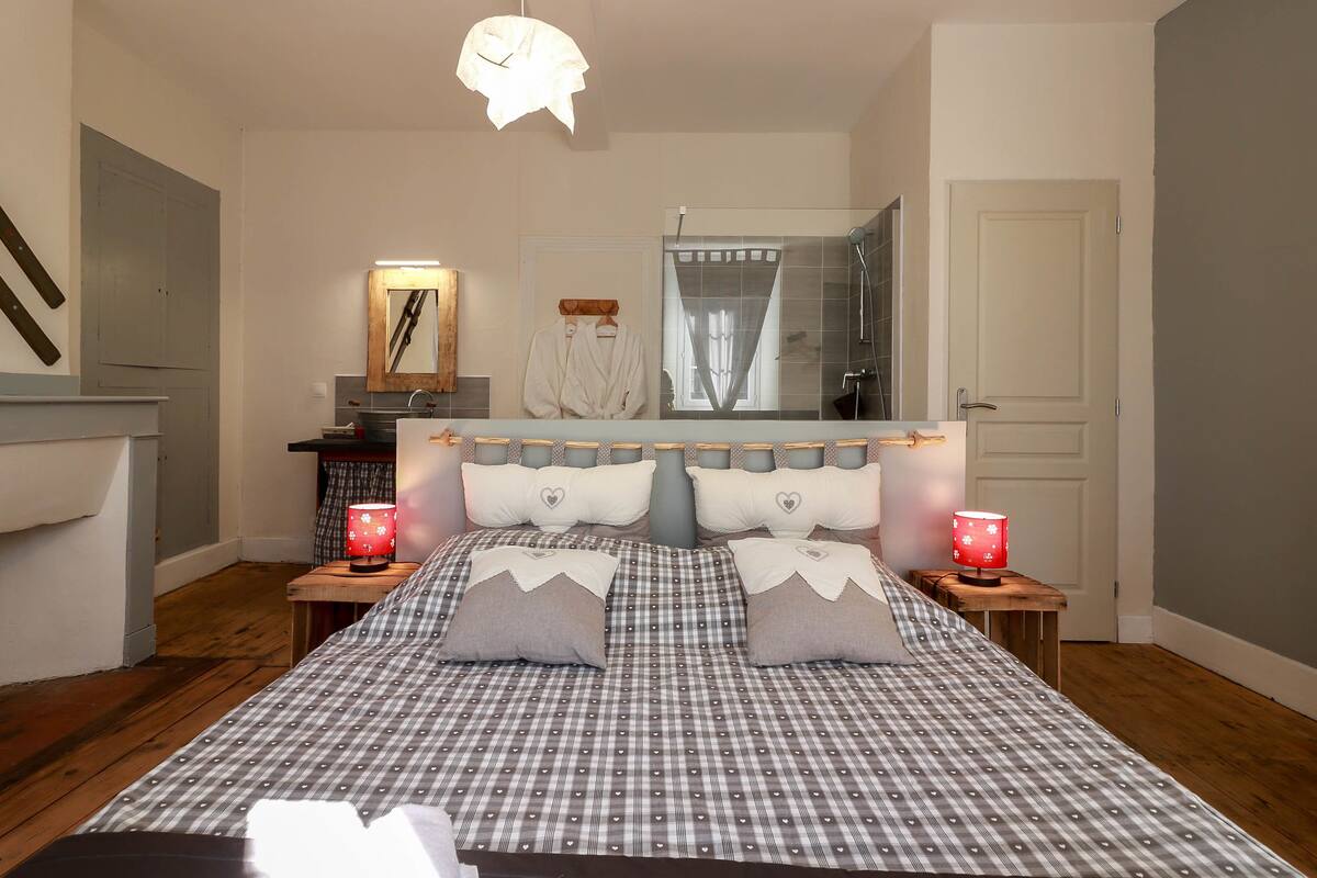 A bedroom with a large bed, a wooden headboard, two bedside tables with lamps, a mirror, and a door.