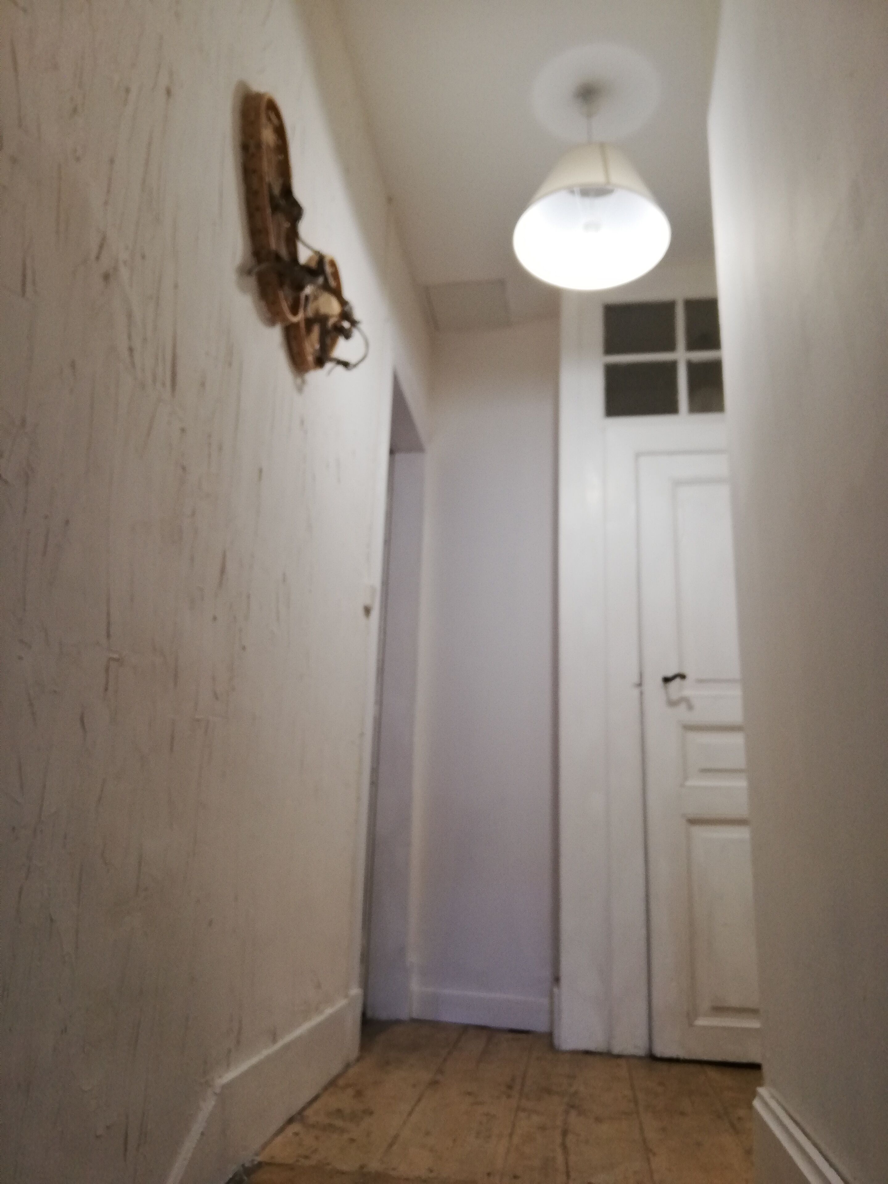 A narrow hallway with a wooden floor, white walls, and a white door at the end.