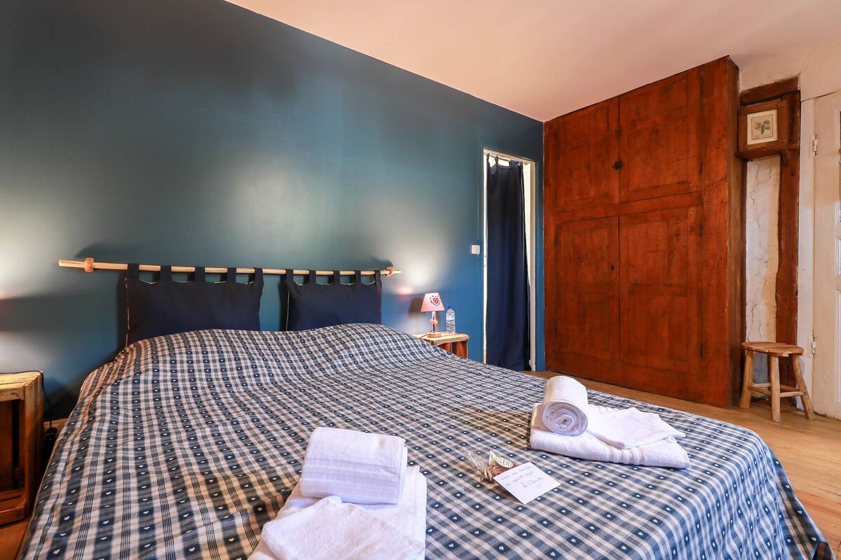 A neatly made bed with a checkered bedspread, a wooden headboard, and a wooden floor.