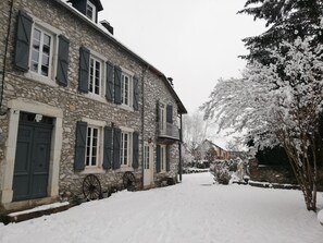 A stone building with shutters, a snow-covered path, and a snow-laden tree. - Domaine des 3 Marmottes (Cierp-Gaud)