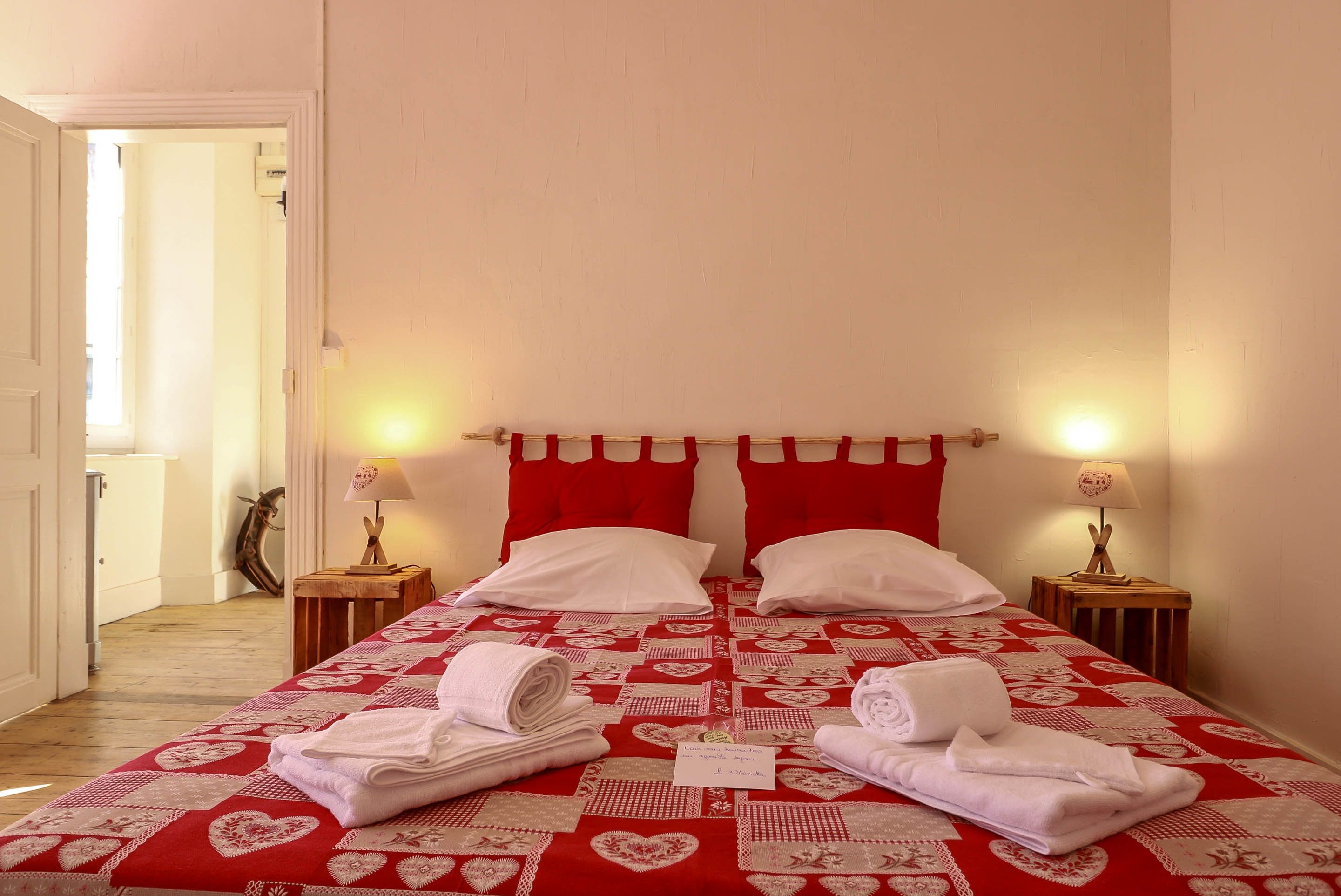 A neatly made bed with red and white bedding, two bedside lamps, and a small table with a lamp.