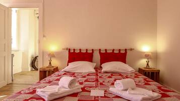 A neatly made bed with red and white bedding, two bedside lamps, and a small table with a lamp.