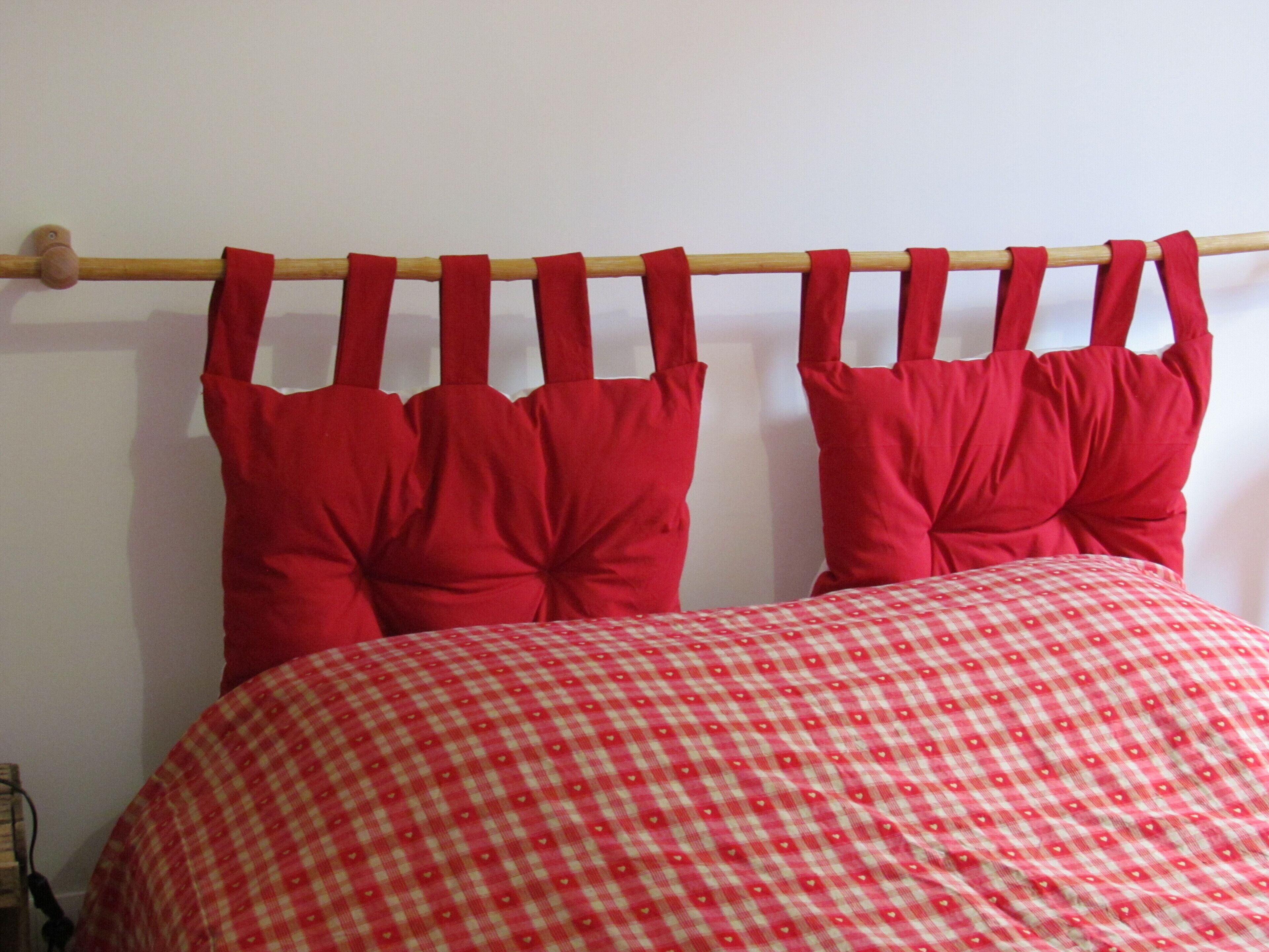 A bed with a red checkered bedspread and red pillows.