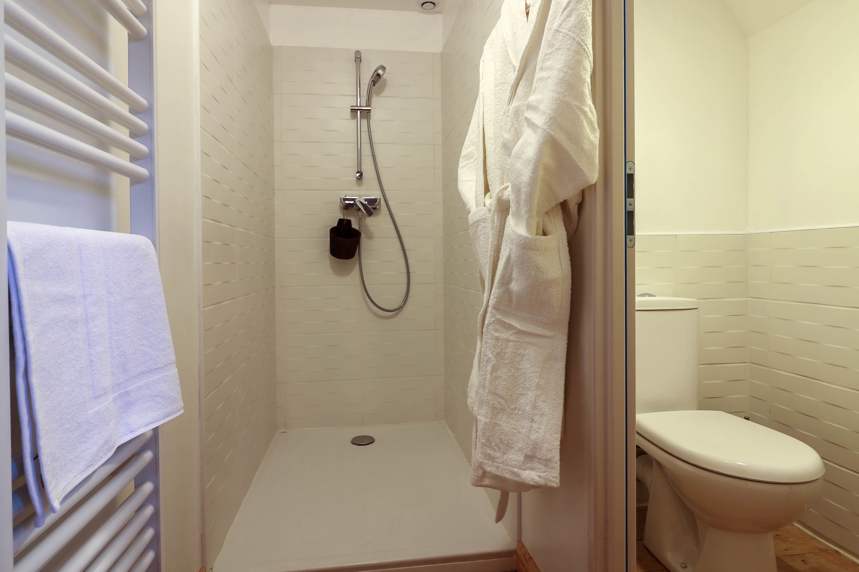 Et lille badeværelse med hvide vægge, brusebad, toilet og håndklædestang.