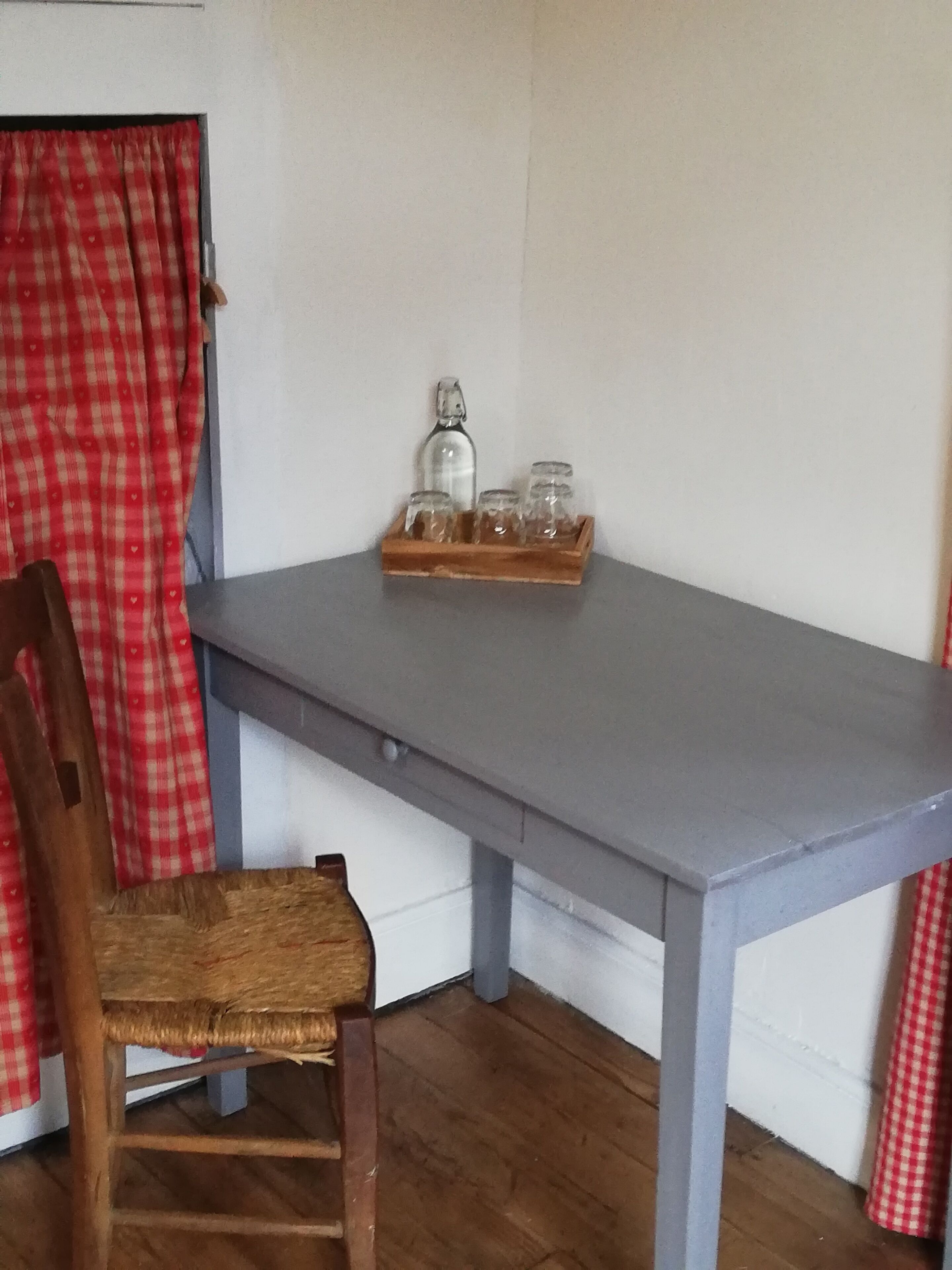 En træstol med flettet sæde, et gråt bord og en bakke med krukker og en flaske på bordet.