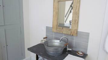 Un baño con espejo de marco de madera, lavabo metálico y pileta blanca.