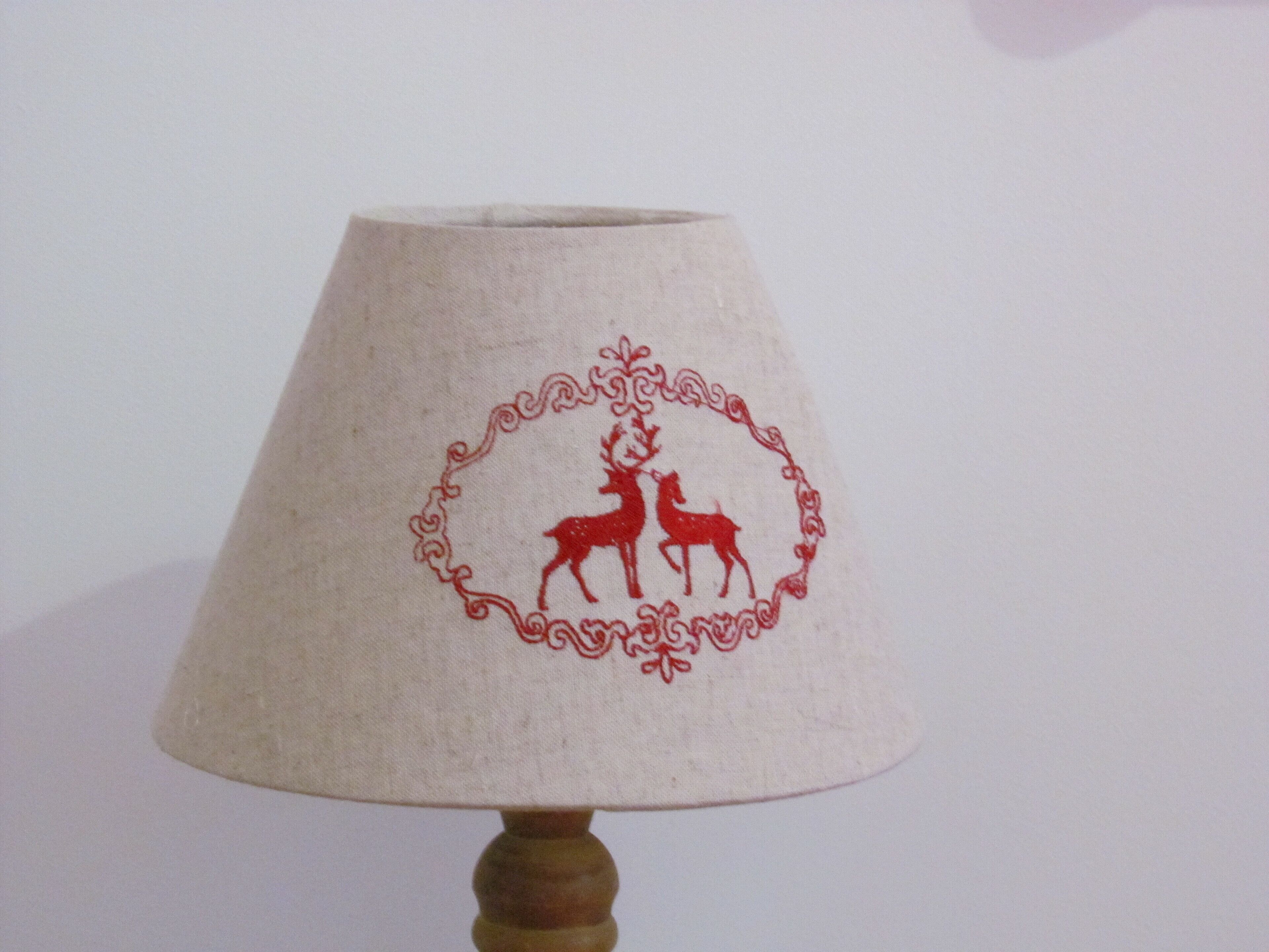 A lamp with a white lampshade featuring a red embroidered deer and floral design.