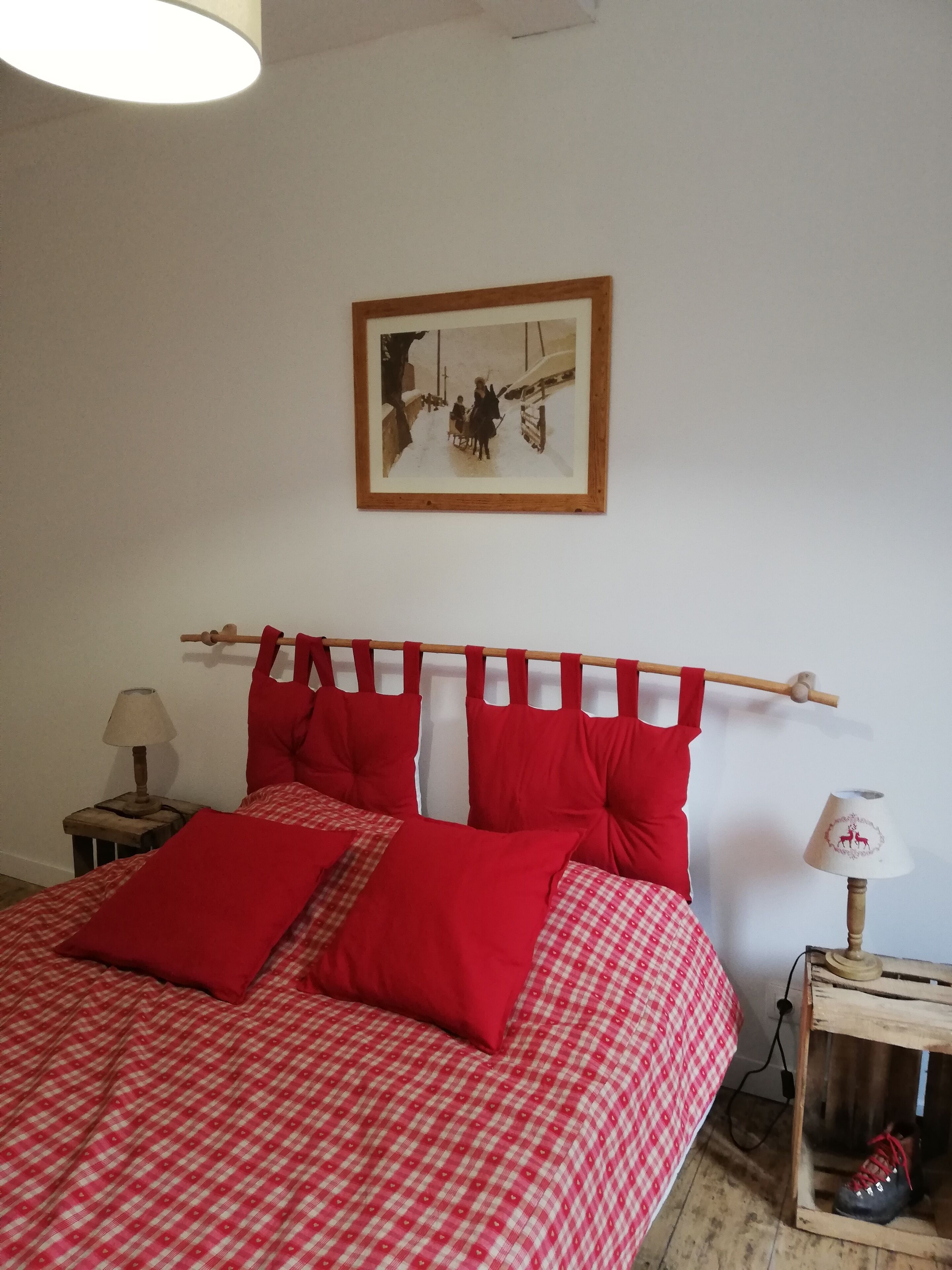 Una cama con ropa de cama a cuadros rojos y blancos, un cabecero de madera y un cuadro en la pared.