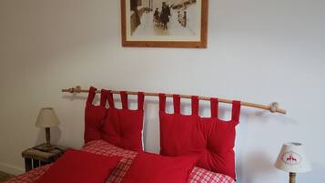 Una cama con ropa de cama a cuadros rojos y blancos, un cabecero de madera y un cuadro en la pared.
