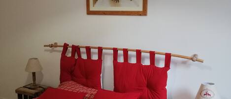 Una cama con ropa de cama a cuadros rojos y blancos, un cabecero de madera y un cuadro en la pared.