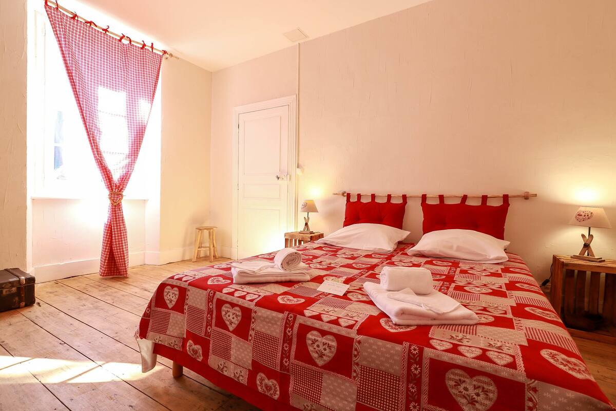 A bedroom with a red and white quilted bedspread, a white door, and a wooden floor.