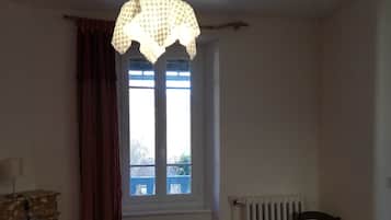 Ein Schlafzimmer mit Bett, Stuhl, Heizkörper und einem Fenster mit Vorhängen.