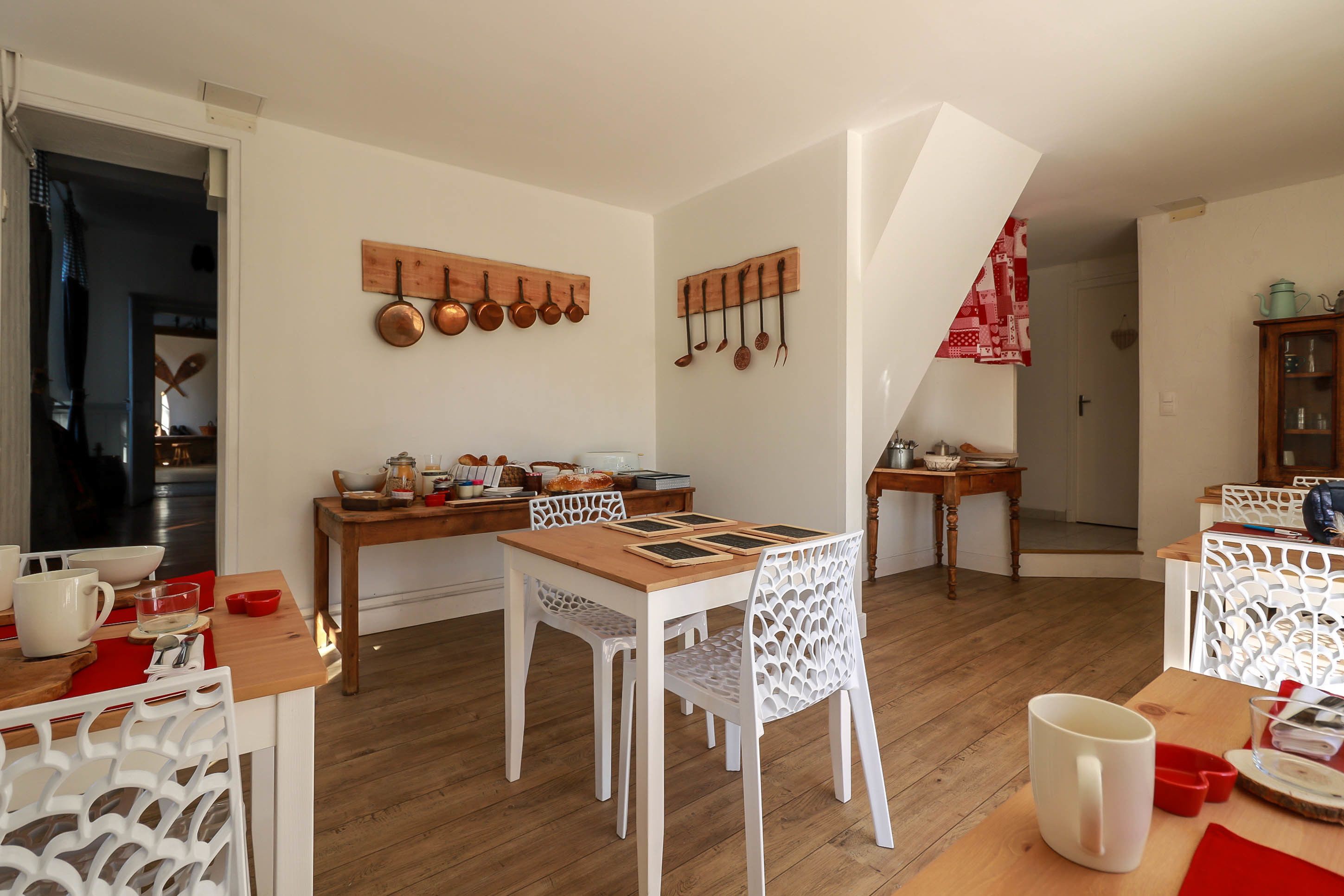 A dining area with a wooden table, white chairs, and a kitchen area with hanging pots and pans.