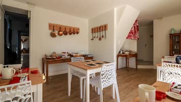 A dining area with a wooden table, white chairs, and a kitchen area with hanging pots and pans.