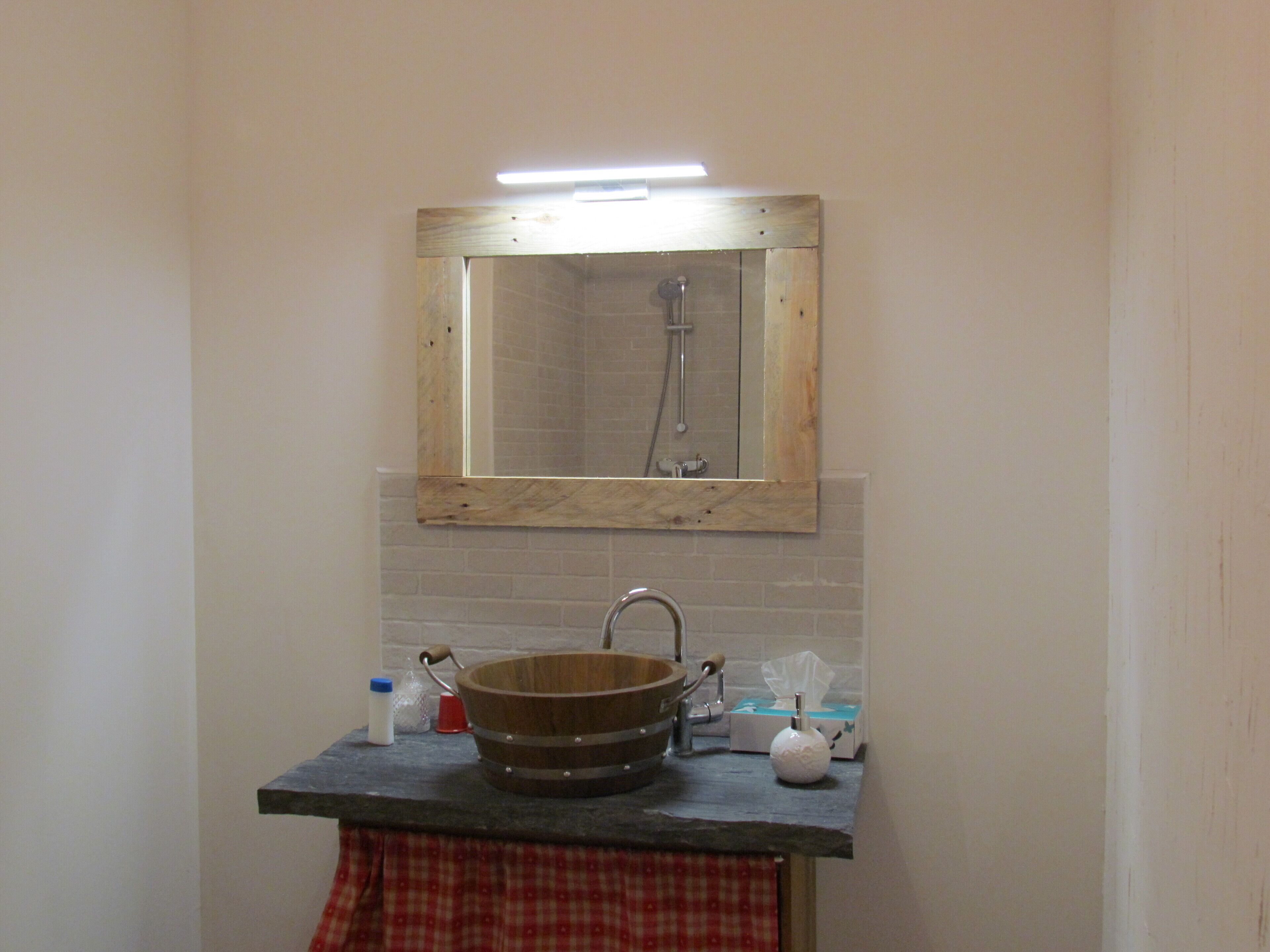 A bathroom with a wooden-framed mirror, a sink with a wooden basin, and a towel hanging on a rack.