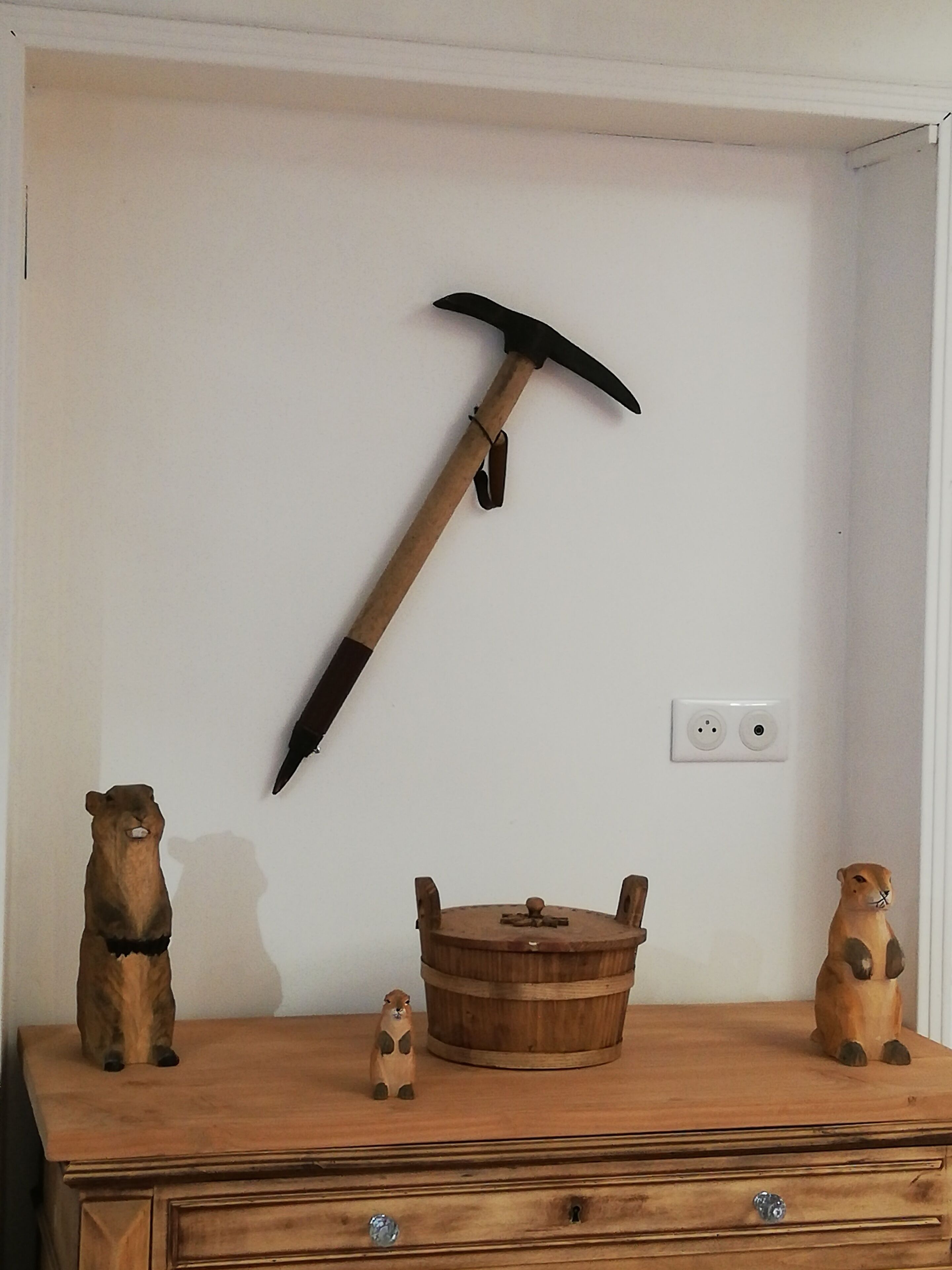 A wooden dresser with a rustic design, a wooden bucket, and two wooden figurines on top.