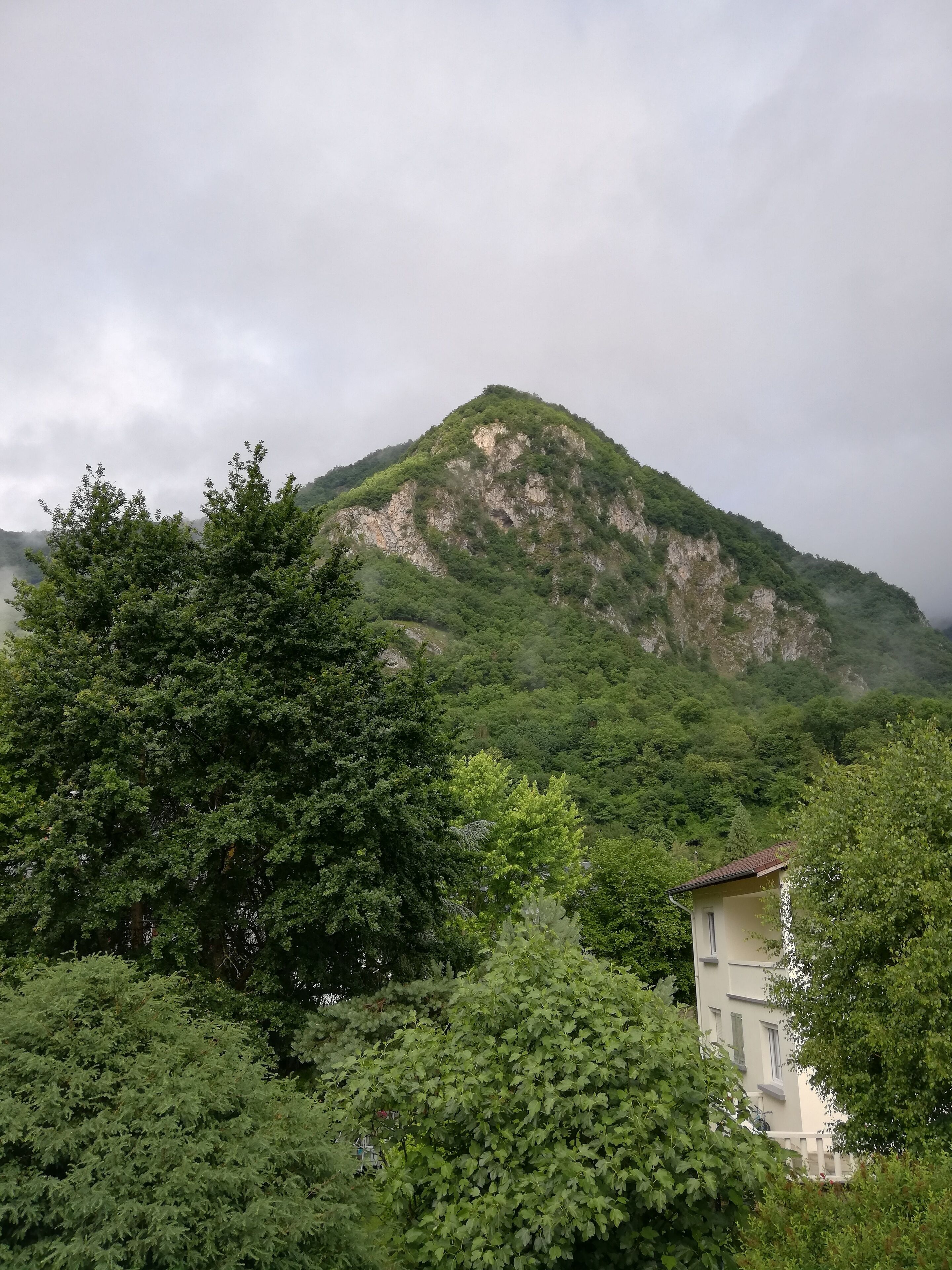 Une montagne couverte d’une végétation luxuriante et verdoyante, avec un petit bâtiment à toit rouge en premier plan.